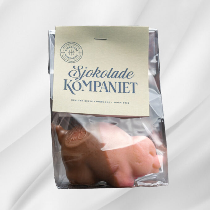 Bilde av liten marsipangris – formet figur i marsipan, dyppet i lys melk- og karamellsjokolade og stemplet med “God Jul”, perfekt som julegodt eller premie til mandelfinneren.